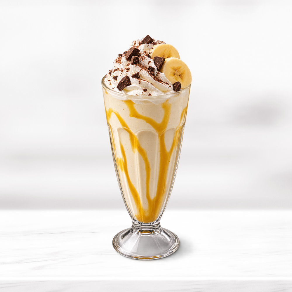 Creamy banana milkshake with whipped cream, banana slices, chocolate pieces and syrup drizzle